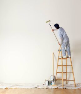 A man on top of a ladder painting the wall.